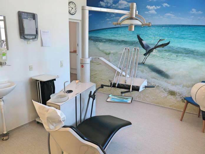Klinik med tandlægestol med forskelligt udstyr og vægtapet af en strand med en fiskehejre.